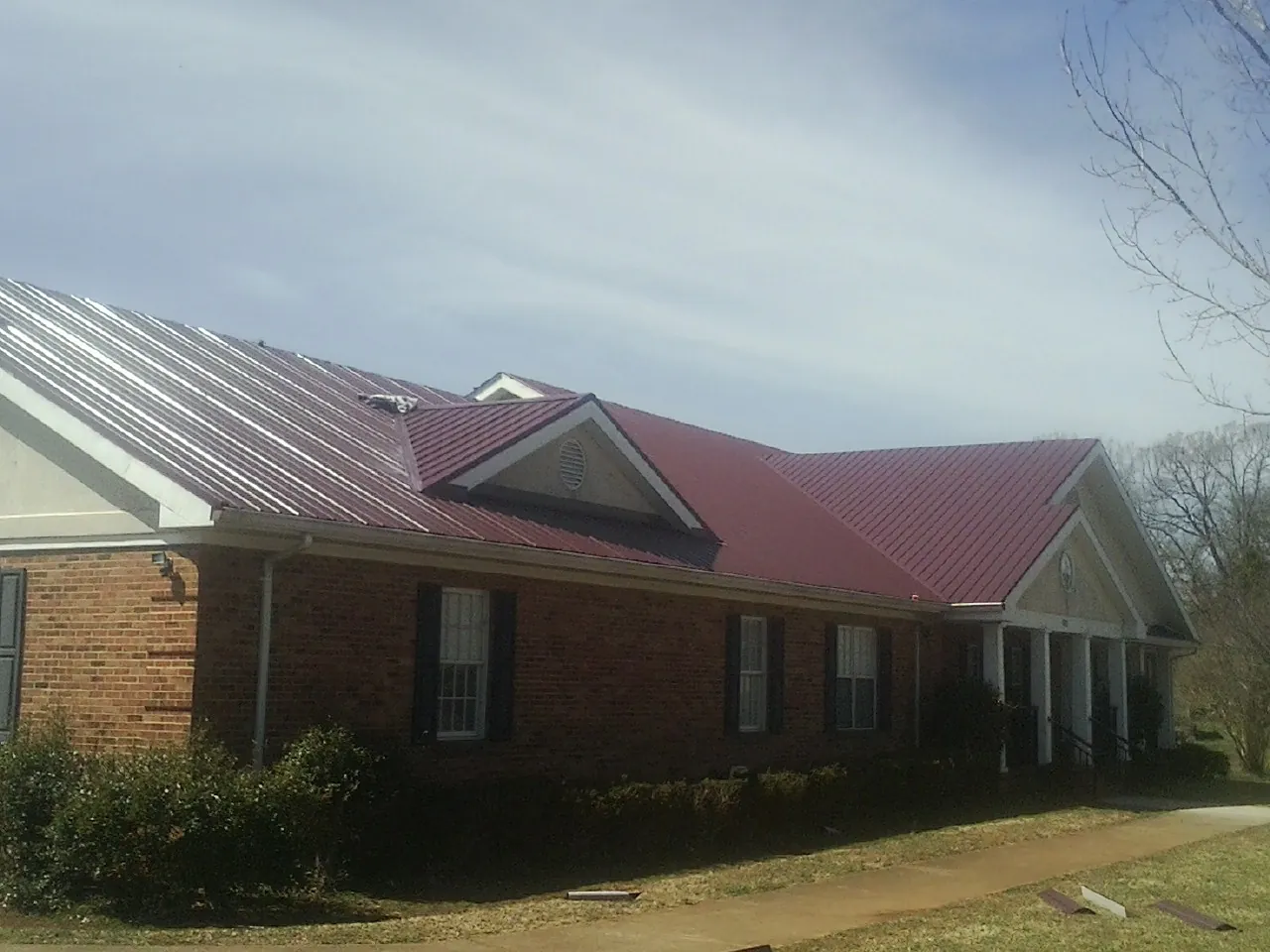 Red metal roof with gabled entries on a long brick building, from a Hail Damage Roof Repair job in Peabody