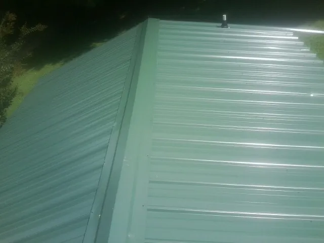 New green metal panels meeting at the ridge of a roof — Flat Roof Repair work by our crew in Peabody