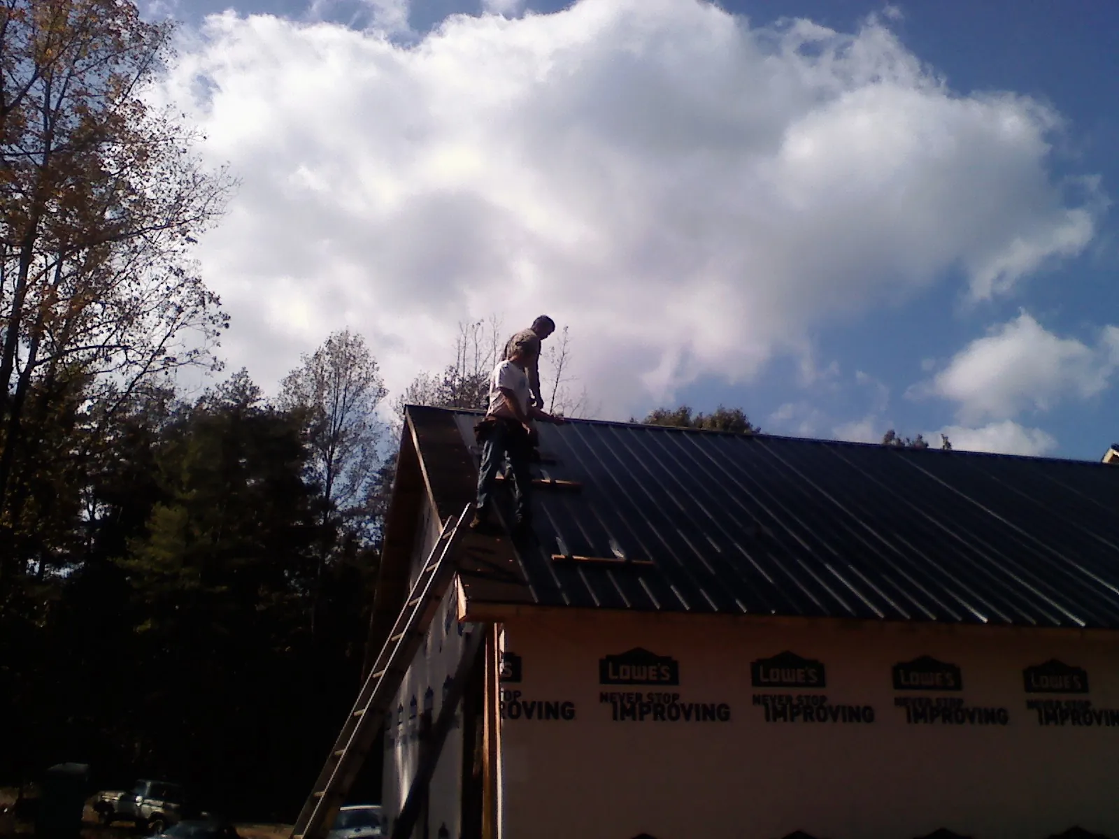 Roofer fastening dark metal panels high against a cloudy sky, from a Roof Inspection job in Peabody