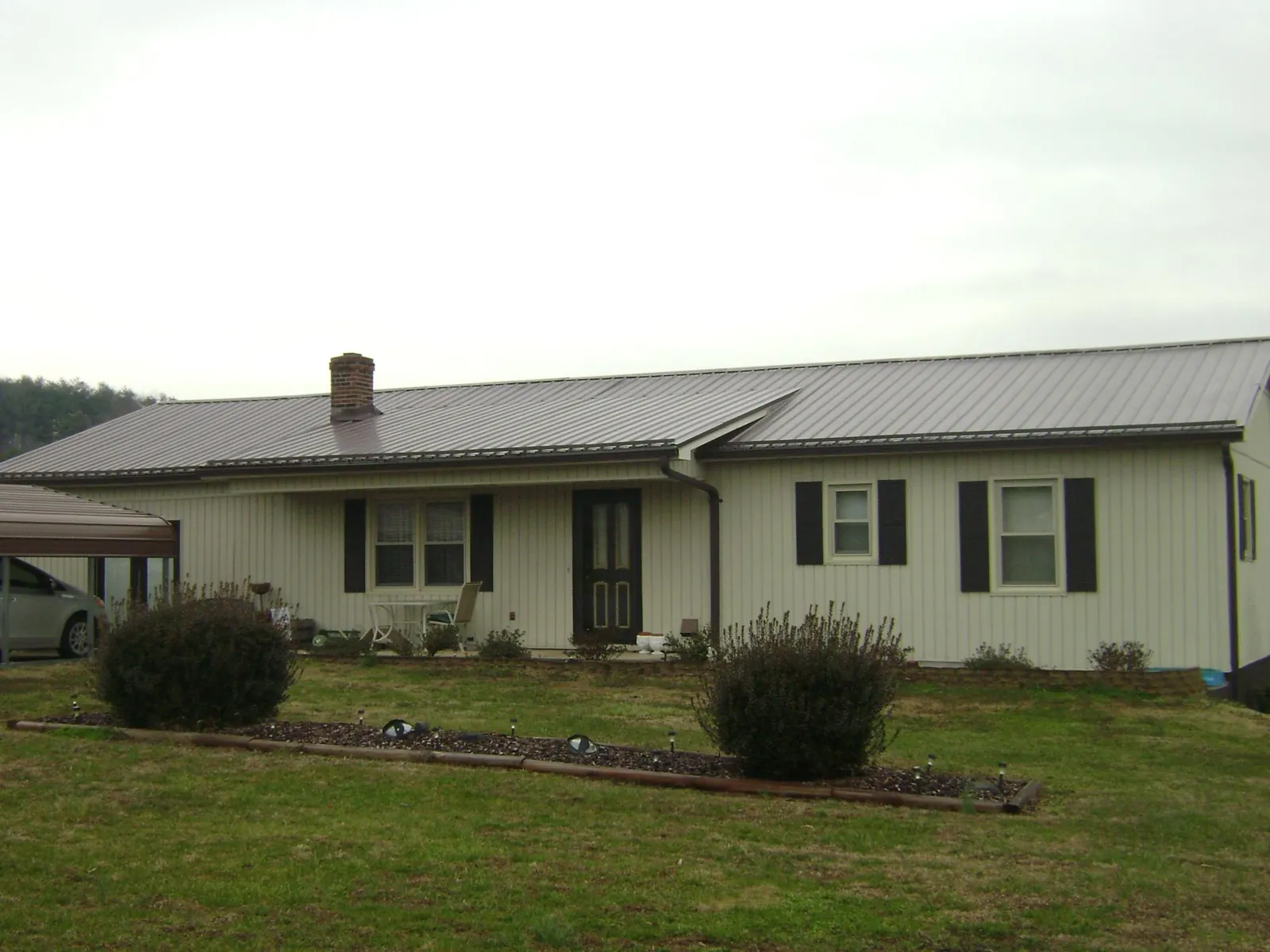 Brown metal roof on a cream sided ranch home with a brick chimney in Peabody