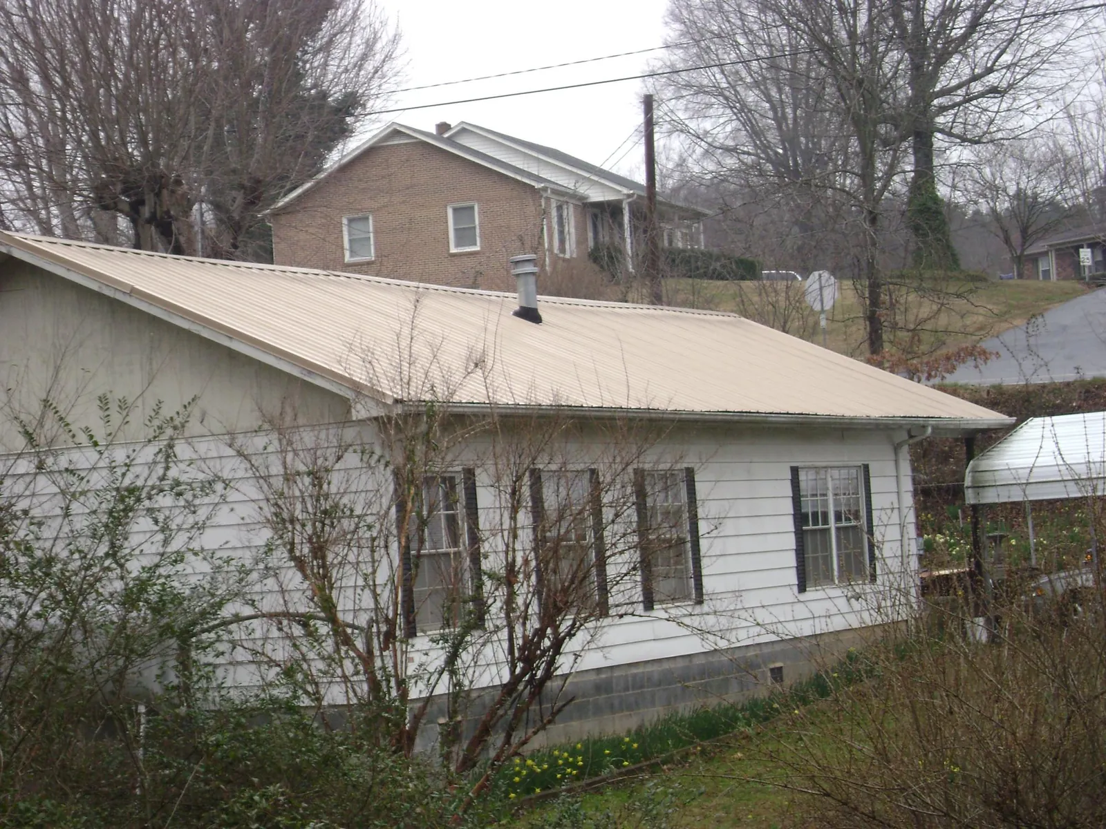 Tan metal roof on a white sided house set into a hillside — Commercial Roofing by Roofing Brothers in Peabody