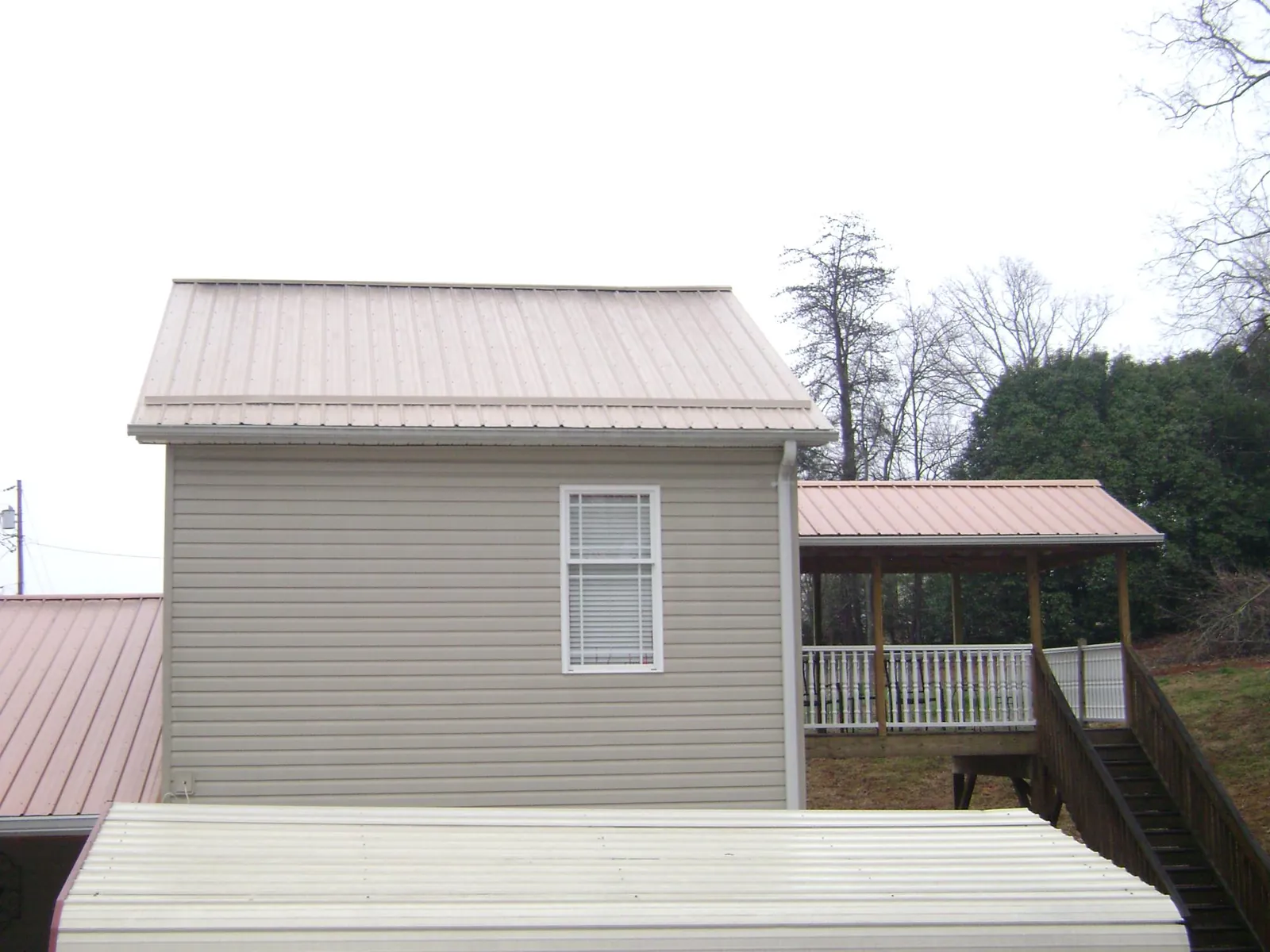 Tan metal roofs on a two story addition and attached porch, from a Roof Replacement job in Peabody